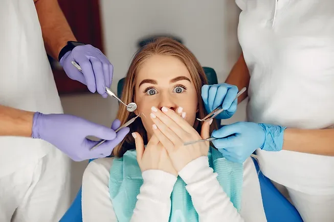 Odontofobia: imagem ilustrativa de um paciente com medo, sentado na cadeira do dentista que realiza o procedimento com auxílio de assistentes.