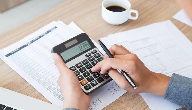 Bitributação: imagem ilustrativa de um profissional fazendo contas com uma calculadora, papéis e caneta.